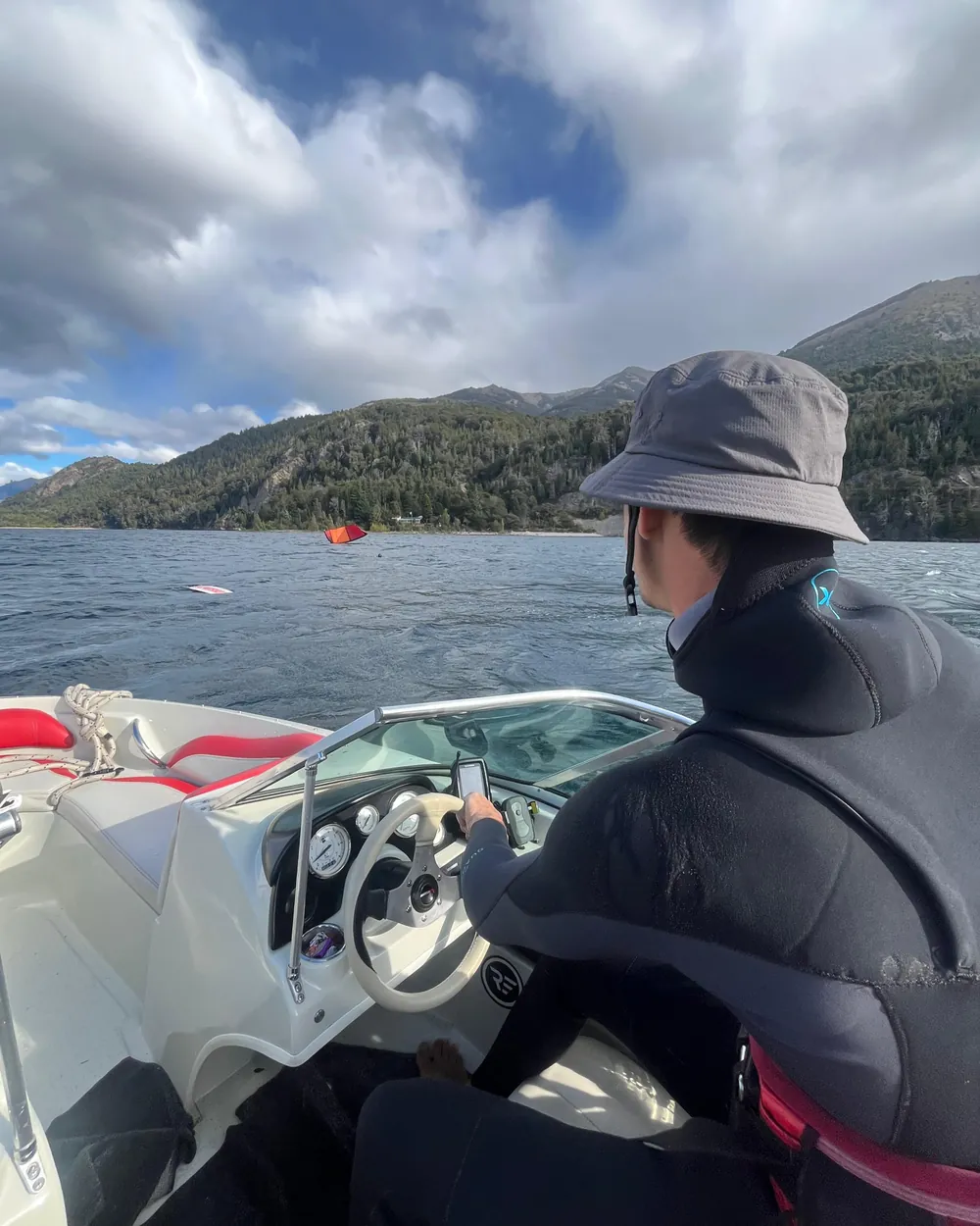 Persona al timón de la embarcación, vista desde atrás, con el lago y la costa boscosa de fondo